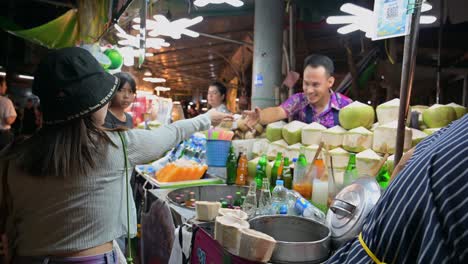 Woman-handing-her-payment-to-the-vendor-for-the-coconut-juice,-while-the-man-on-the-right-is-arranging-the-opened-chilled-coconuts-in-the-container