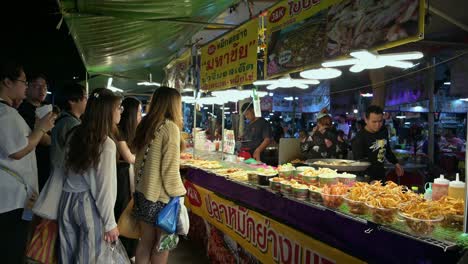 Un-Entusiasta-Grupo-De-Turistas-Esperando-Sus-Pedidos-De-Alimentos-Fritos-De-Los-Vendedores-Ambulantes-En-El-Mercado-De-Fin-De-Semana-De-Chatuchak,-Bangkok,-Tailandia