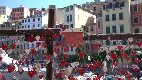 Beautiful-romantic-red-and-white-card-hearts-tie-onto-the-fishing-nets-on-the-harbour-wall-against-the-background-of-the-colourful-houses-in-Port-of-Liguria,-Camogli,-Italy