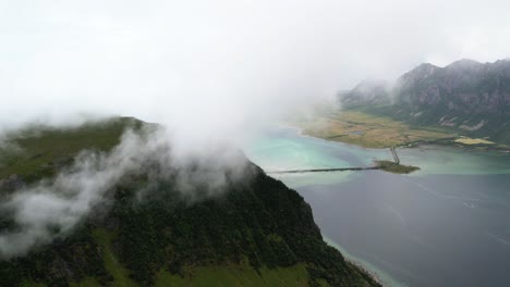 Clouds-surrounding-a-mountain-with-tropical-water-beneath-it-in-Lofoten,-Norway