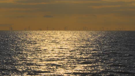 Wind-turbines-on-horizon-at-dusk-with-sparkling-sea