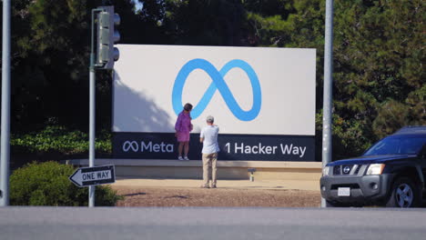 Tourists-posing-for-photograph-with-the-meta-sign,-1-hacker-way-entrance-to-Menlo-park-headquarters,-California