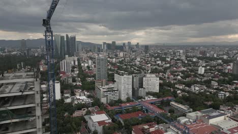 Aerial-flyby:-Building-construction-tower-crane-in-cloudy-Mexico-City
