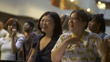 Two-asian-woman-having-amusing-conversation-during-live-ethnic-music-festival,-filmed-as-closeup-slow-motion-shot