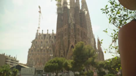 Stunning-video-of-a-young-caucasian-female-in-a-green-dress-with-a-knitted-hat,-observing-incredible-landmark-building---Sagrada-Familia,-Barcelona