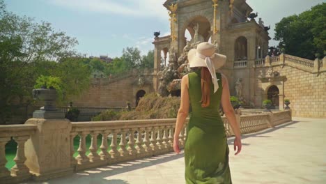 Stunning-footage-of-a-young-caucasian-girl-in-a-green-dress-and-hat-walks-joyfully-in-front-of-Cascada-Monumental---Gaudí's-fountain-in-Parc-de-la-Ciutadella