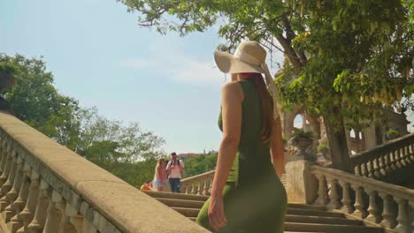 Atemberaubende-Aufnahmen-Eines-Mädchens-In-Einem-Grünen-Kleid-Mit-Hut,-Das-Die-Treppe-Hinaufgeht-Und-Freudig-Den-Brunnen-Der-Cascada-Monumental-Gaudi-Und-Den-Parc-De-La-Ciutadella-Betrachtet