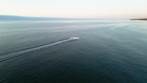 Experience-the-thrill-of-a-jetski-gliding-along-the-Baltic-Sea-shore-at-sunset,-captured-in-stunning-detail-by-a-drone