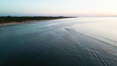 Experience-the-thrill-of-a-jetski-gliding-along-the-Baltic-Sea-shore-at-sunset,-captured-in-stunning-detail-by-a-drone