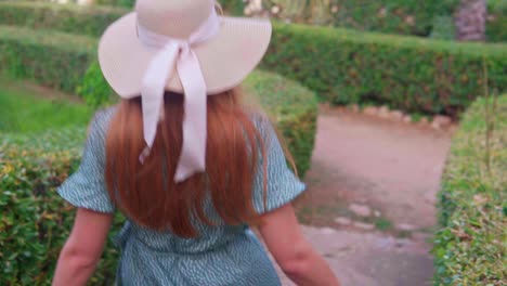 Stunning-video-of-young-caucasian-girl-in-a-green-dress-with-knitted-hat-happily-walking-along-a-green-pathway