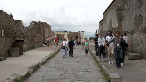 A-slow-motion-shot-of-a-tour-guide-sharing-knowledge-of-the-area-as-the-group-of-tourists-walk-down-an-ancient-street-surrounded-by-ruins-in-Pompeii,-Italy