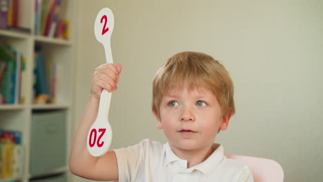 Attentive-little-boy-raises-number-fan-during-maths-lesson