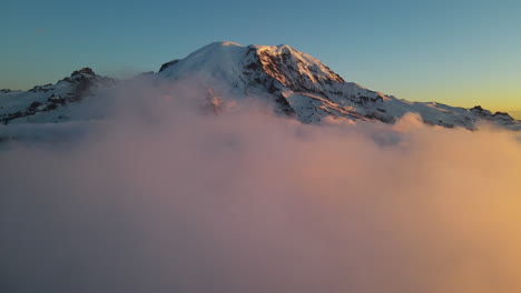 Aerial-drone-view-of-the-mountain-summit-of-Mount-Rainier-volcano-above-the-clouds-at-sunset,-beauty-in-nature