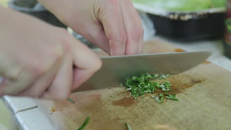 Person-using-sharp-chef-knife-to-cut-pieces-of-rosemary-leaves-for-cooking