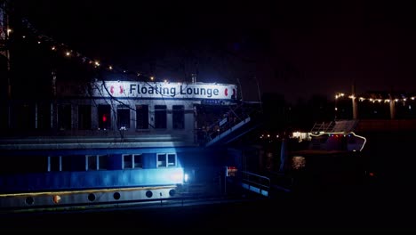 Floating-lounge-boat-docked-in-Spree-river-in-Berlin-at-night,-static-shot