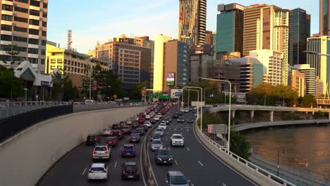 Dynamic-zoom-out-shot-capturing-rush-hour-inbound-and-outbound-vehicle-traffics-on-M3-Pacific-Motorway-with-riverside-downtown-cityscape-in-the-background-at-sunset-golden-hours