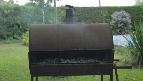 Metal-barbecue-barrel-with-smoking-coal-roasting-meat-inside-in-a-summer-day