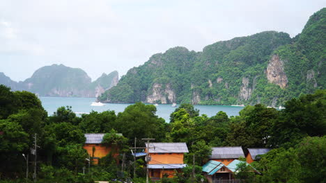 Wide-shot-showing-Beautiful-coastline-and-mountains-of-Thailand,-view-from-Koh-Phi-Phi-Island---Cruising-boat-and-local-houses-on-island