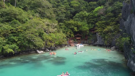 Tourists-kayaking-in-tropical-emerald-Cadlao-Lagoon,-El-Nido,-Karst-rock-formations-at-Island,-Philippines,-Aerial-view