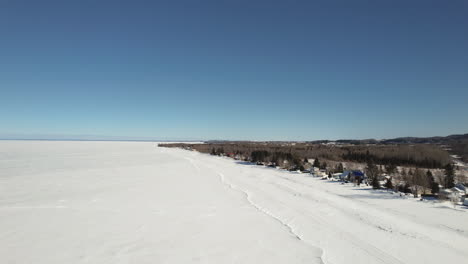 Flying-drone-above-houses-and-a-frozen-lake-during-winter-in-canada