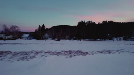 Flying-drone-filming-beachhouses-by-a-frozen-lake-during-winter-in-Canada