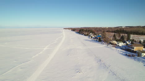 Fliegende-Drohne-über-Häusern-Und-Einem-Zugefrorenen-See-Im-Winter-In-Kanada
