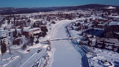 4K-Drone-Video-of-People-Walking-Across-Pedestrian-Bridge-over-Frozen-Chena-River-in-Downtown-Fairbanks-Alaska-on-Snowy-Winter-Day