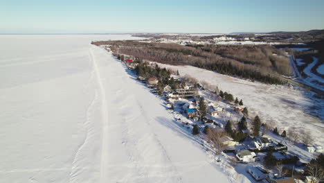 Fliegende-Drohne-über-Häusern-Und-Einem-Zugefrorenen-See-Im-Winter-In-Kanada