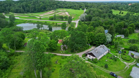Revealing-Drone-View-of-Lush-Green-Homestead-with-Pond-and-Offroad-Track-Visible