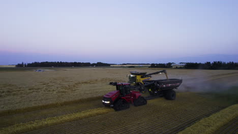 Combine-harvester-unloads-harvested-grain-onto-tractor-trailer,-twilight-aerial