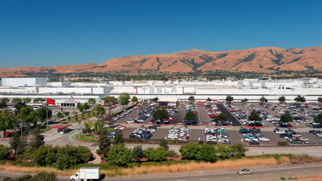 Aerial-view-approaching-huge-TESLA-electric-car-showroom-in-Fremont,-California-under-mountain-landscape