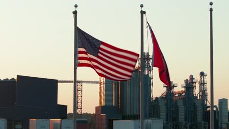 A-USA-and-Arkansas-flag-wave-in-the-wind-at-sunset-with-a-rice-manufacturing-plant-in-the-background