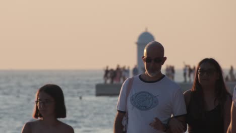 People-walking-Zadar-promenade-at-sunset-with-lighthouse-and-more-people-in-background