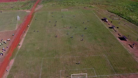 Drone-orbit-around-football-players-walking-onto-pitch-revealing-other-nearby-football-pitches---players-train-on-the-side-line