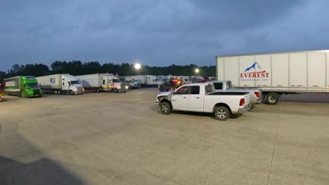 tractor-trailer-or-semi-truck-leaving-a-parking-spot-in-the-large-vehicle-parking-lot-at-a-truck-stop-at-dusk