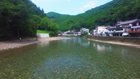 Aerial-shot-from-drone-reveals-Koyasan-village-river,-moving-closer-to-people-engaged-in-serene-river-bathing