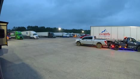 Tow-vehicle-connecting-to-a-pickup-truck-and-backing-pickup-truck-into-a-parking-space-at-a-truck-stop-at-dusk