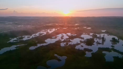 Glowing-sunrise-above-swampy-lake-landscape,-aerial-ascend-view