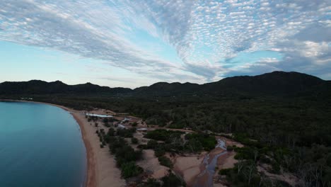 ascending-drone-shot-over-horseshoe-bay-beach-in-Magnetic-Island-at-sunset-with-clouds-in-the-sky,-Queensland,-Australia