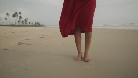 Woman-feet-in-a-red-dress-standing-on-the-sea-beach-with-the-wind-blowing---Beautiful-scene-of-a-suntanned-pretty-woman-in-a-red-dress-bare-feet-on-an-ocean-beach
