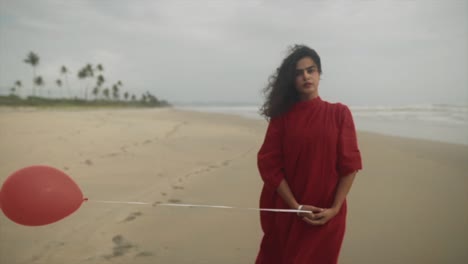 Indian-girl-with-a-red-balloon-in-hand-wearing-a-readdress-stands-on-the-sea-beach-with-wind-blow