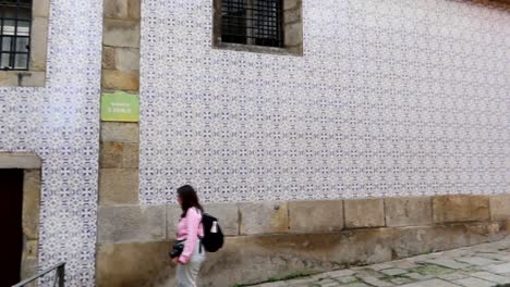 Tourist-woman-walking-in-front-of-St-Nicholas-Church-wall-facade-in-Porto