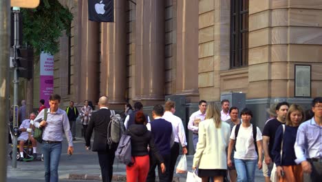 Dynamic-zoom-in-shot-capturing-large-swarm-of-people-crossing-the-road-at-the-corner-of-Queen-and-Edward-street-during-rush-hours,-Brisbane-Apple-flagship-store-at-heritage-listed-MacArthur-Chambers