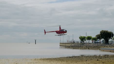 Helicóptero-Rojo-Aterrizando-En-La-Laguna-Cairns-Esplanade-En-Un-Día-Nublado-A-Cámara-Lenta-En-Queensland,-Australia