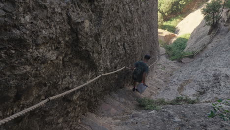 Adventurous-Hiker-Descends-Steep-Stone-Stairs-Alongside-Majestic-Rock-Wall