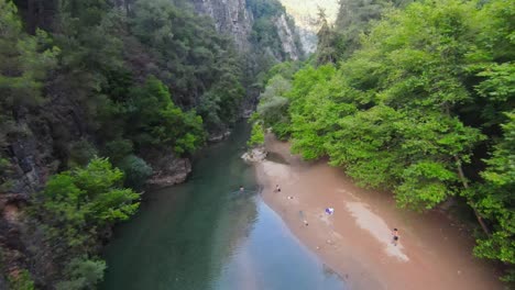 Drone-descends-and-flies-through-river-between-tall-canyon-cliffs