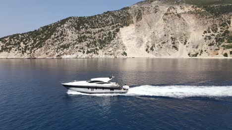 Small-yacht-drives-along-the-scenic-coastline-of-Kefalonia,-Greece-on-sunny-day
