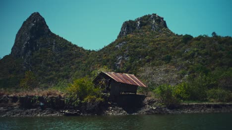 Eine-Kleine-Kaputte-Hütte-Neben-Einem-Fluss-In-Thailand-Mit-Kalksteinhügeln-Im-Hintergrund