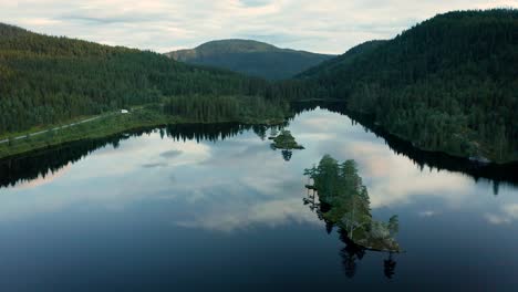 Epic-nature-scene-of-calm-Norwegian-lake-surrounded-by-lush-forest,-aerial