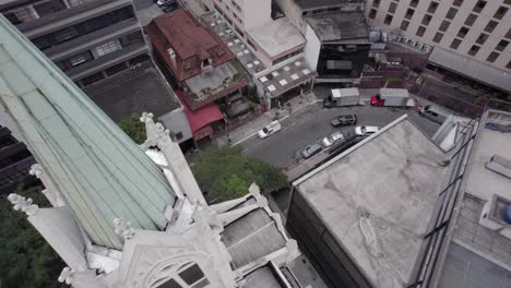 City-aerial-descends-along-church-steeple-to-bar-on-Sao-Paulo-street